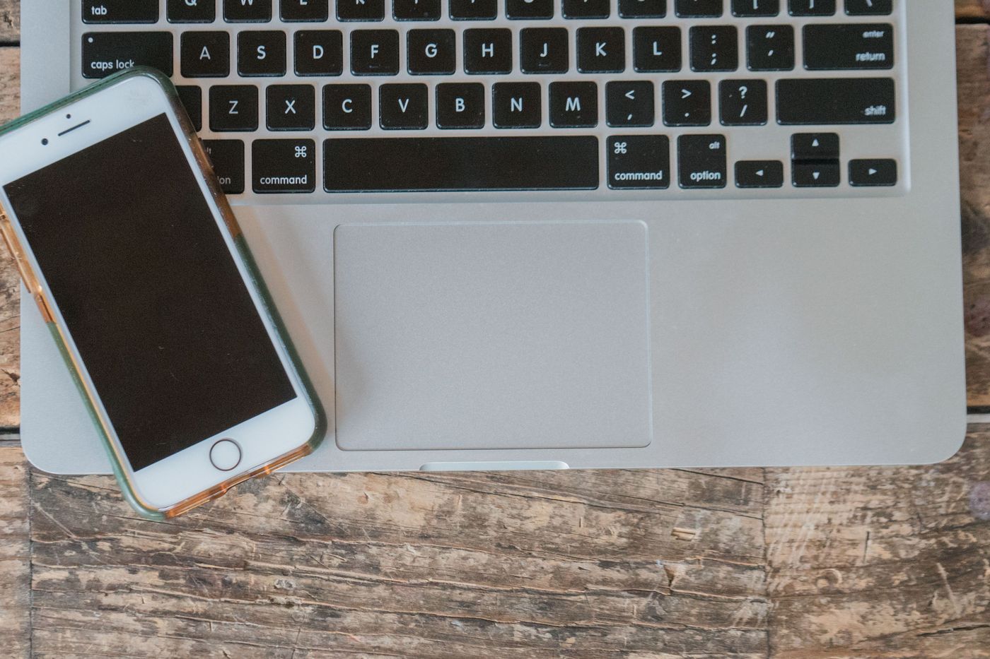 A phone lying on a laptop on a wooden desk.