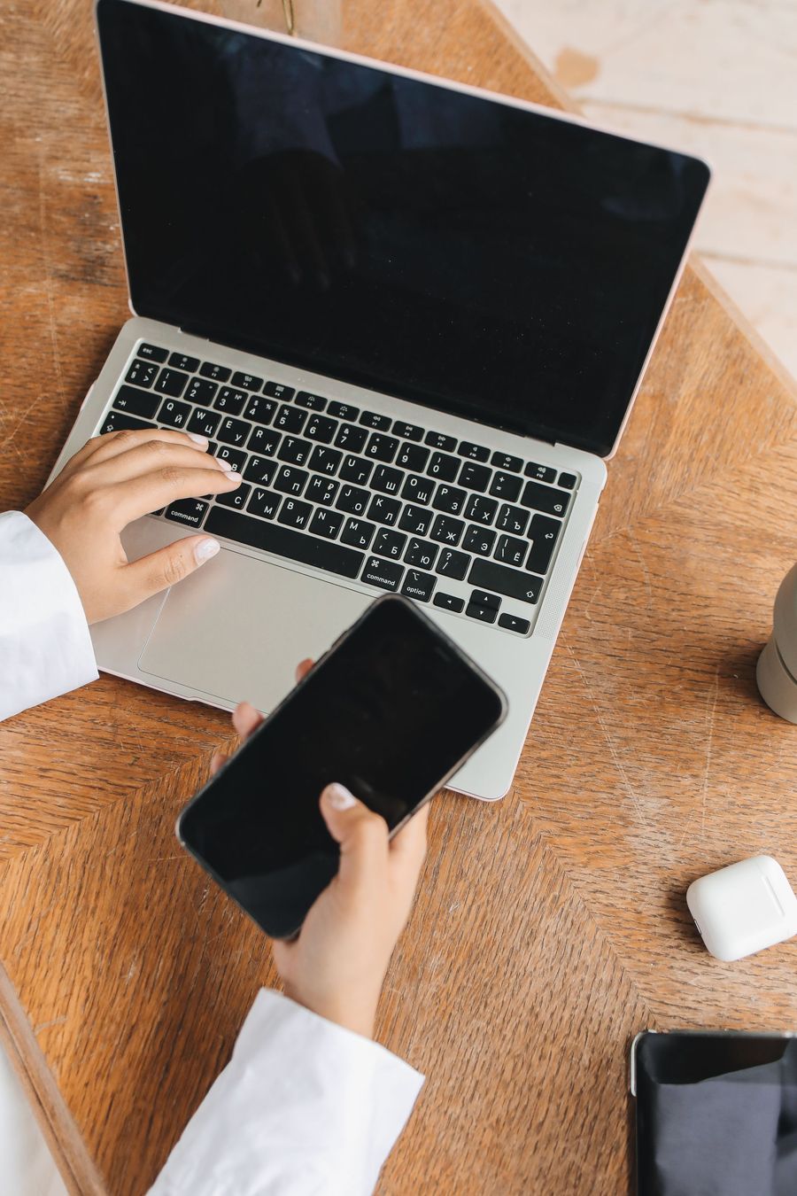 Hands on a laptop keyboard, a phone beside them on a wooden desk.