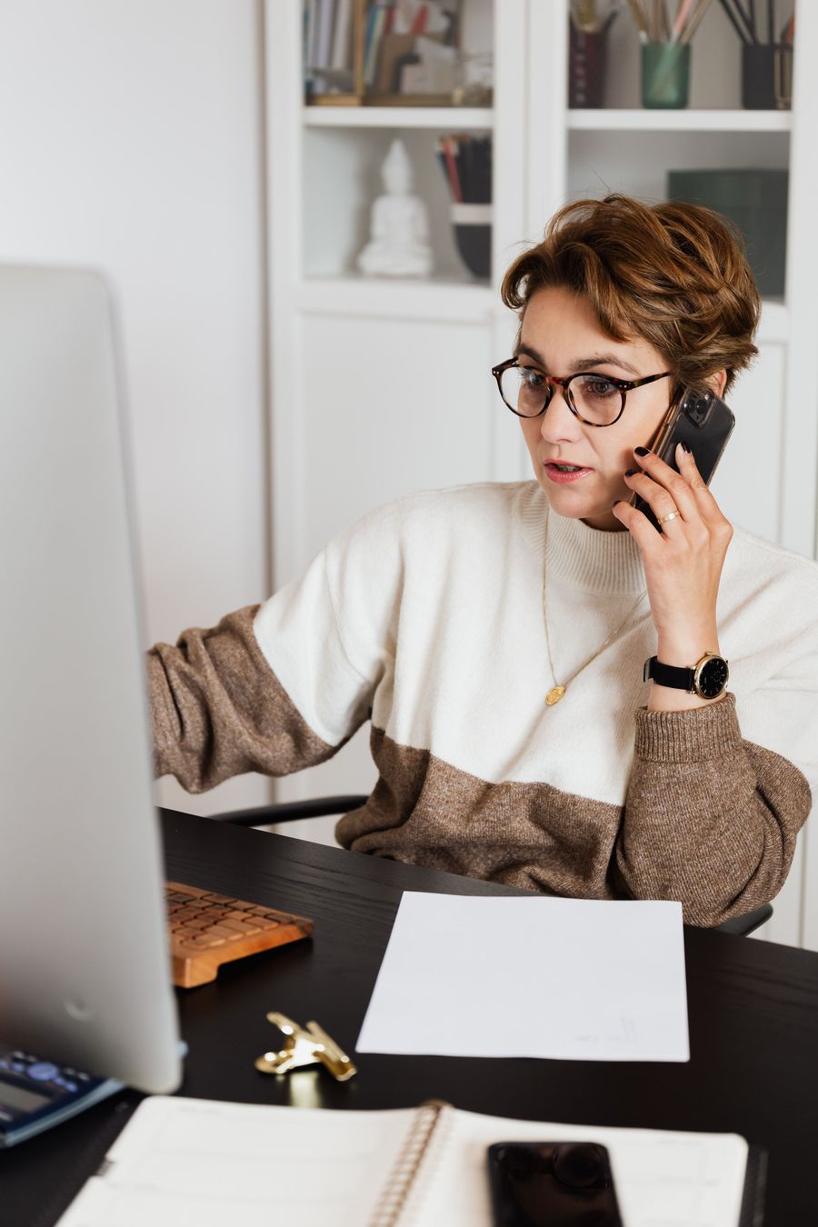 A woman at a desk talking on the phone in front of a monitor.