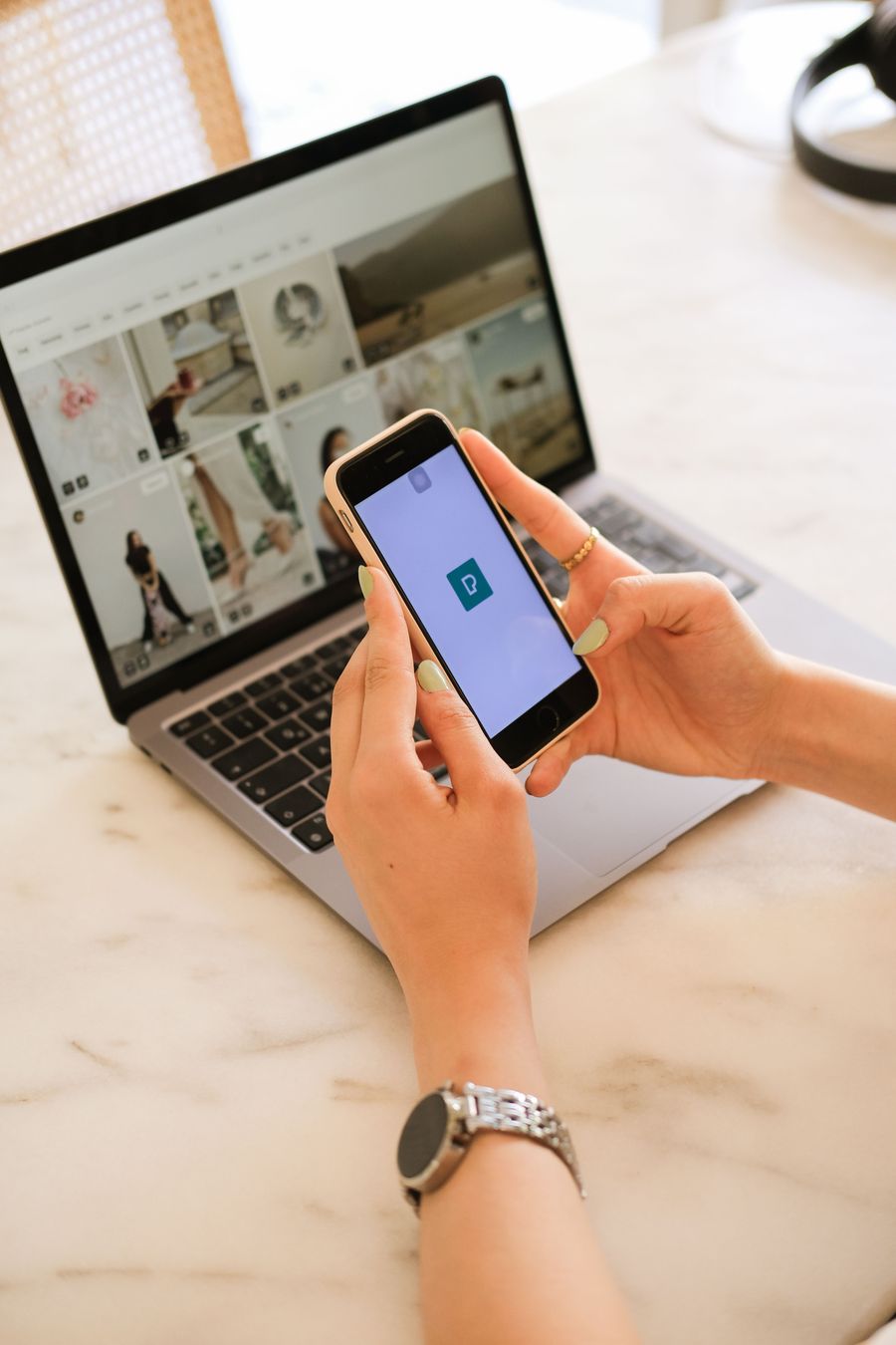Hands holding a phone above an open laptop.